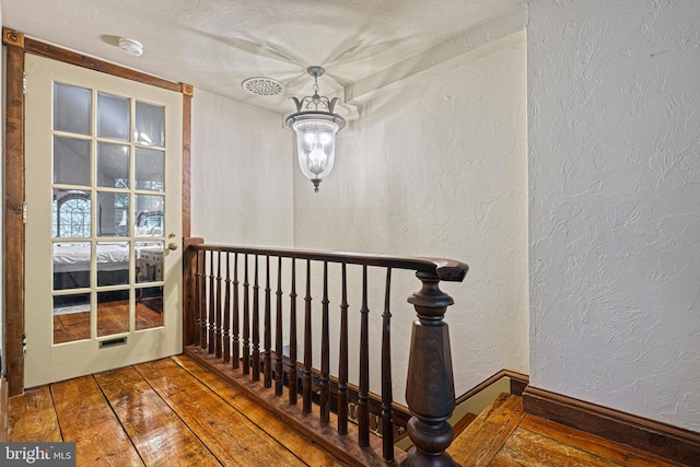 staircase with a textured ceiling, hardwood / wood-style flooring, and a chandelier