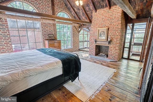 bedroom with high vaulted ceiling, a brick fireplace, brick wall, and hardwood / wood-style floors