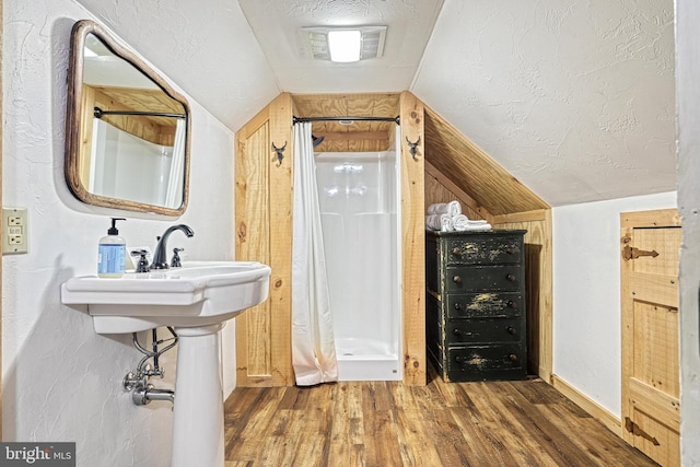 bathroom featuring lofted ceiling, hardwood / wood-style floors, walk in shower, and a textured ceiling