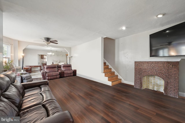 living room with a brick fireplace, a textured ceiling, dark wood-type flooring, and ceiling fan