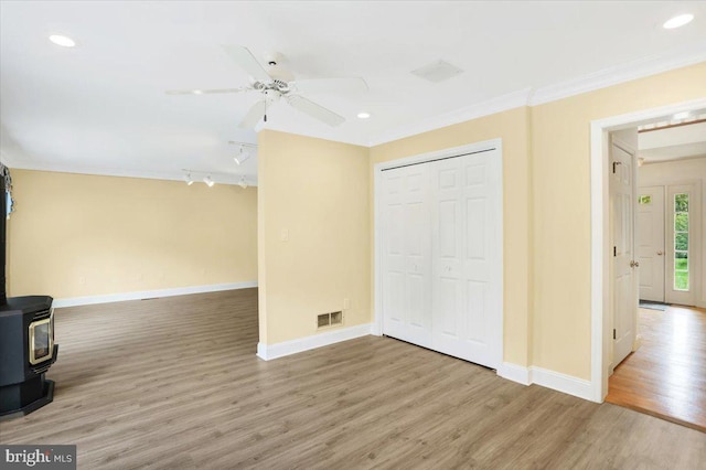 interior space featuring crown molding, a wood stove, wood-type flooring, and ceiling fan