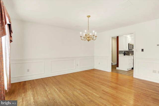 spare room with an inviting chandelier and light hardwood / wood-style flooring