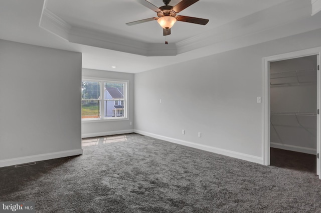 unfurnished bedroom featuring ceiling fan, dark colored carpet, a walk in closet, and a raised ceiling