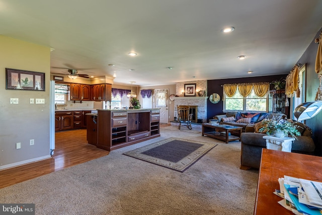 living room with a stone fireplace, wood-type flooring, and ceiling fan