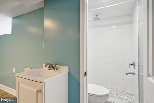 bathroom featuring toilet, hardwood / wood-style flooring, vanity, and a tile shower