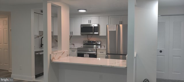 kitchen with white cabinets, sink, light stone countertops, kitchen peninsula, and stainless steel appliances