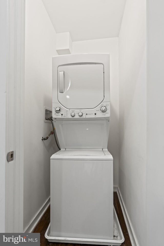 washroom featuring dark wood-type flooring, stacked washer / drying machine, laundry area, and baseboards