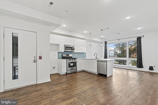 kitchen featuring kitchen peninsula, white cabinets, appliances with stainless steel finishes, dark hardwood / wood-style floors, and pendant lighting