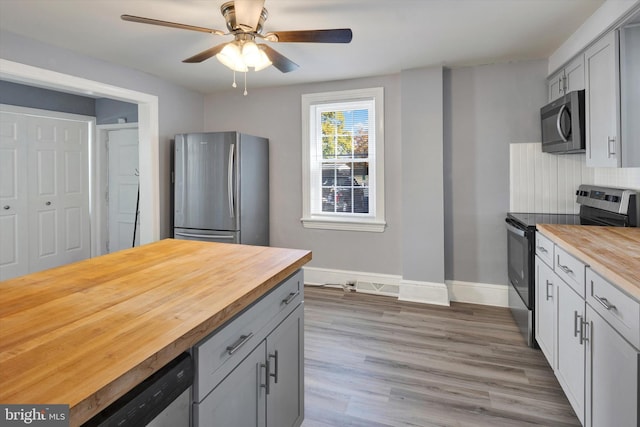 kitchen featuring ceiling fan, appliances with stainless steel finishes, wood-type flooring, gray cabinetry, and wooden counters