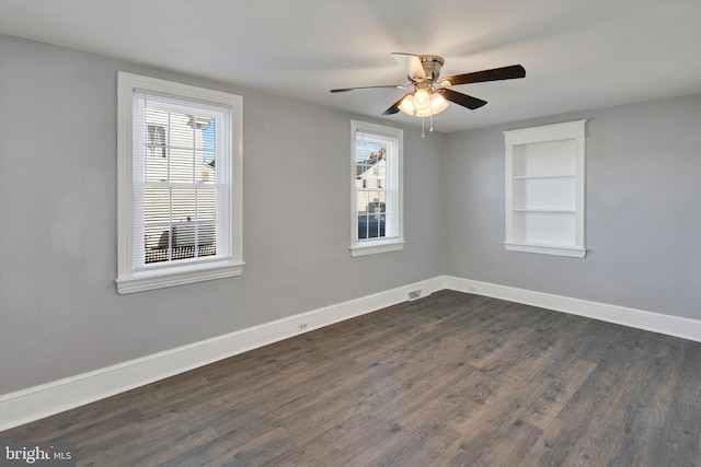 empty room with built in shelves, dark hardwood / wood-style floors, a healthy amount of sunlight, and ceiling fan