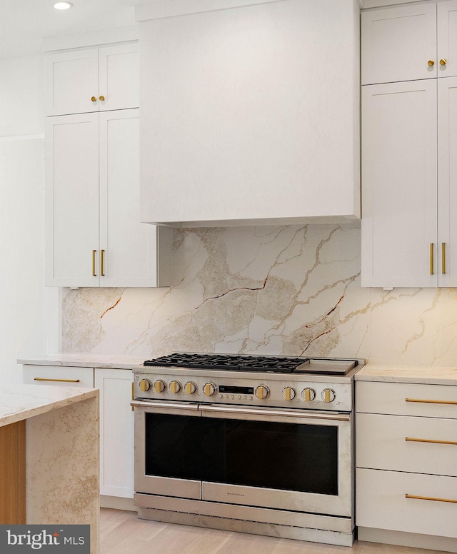 kitchen featuring stainless steel range, light hardwood / wood-style flooring, range hood, white cabinetry, and tasteful backsplash