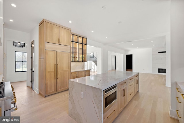 kitchen featuring light stone countertops, stainless steel microwave, light wood-type flooring, and a kitchen island