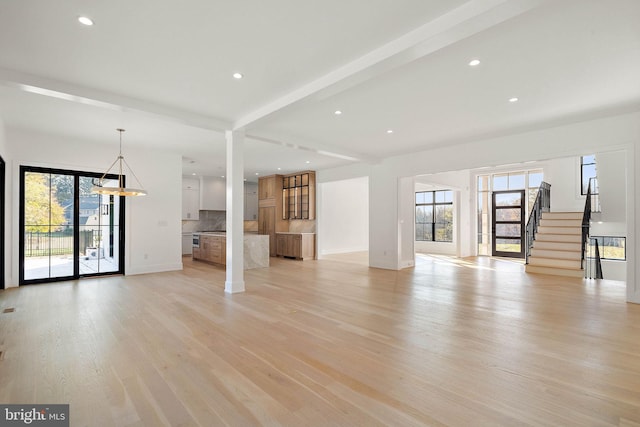 unfurnished living room featuring light hardwood / wood-style floors, beam ceiling, and plenty of natural light