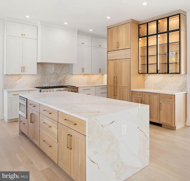 kitchen with a large island, white cabinetry, built in appliances, and light hardwood / wood-style floors