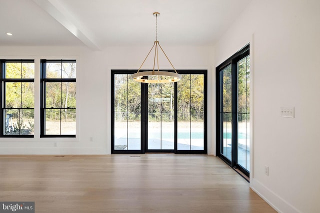 unfurnished dining area featuring a notable chandelier, a healthy amount of sunlight, and light wood-type flooring