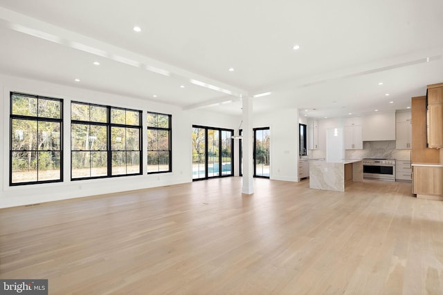 unfurnished living room featuring beam ceiling and light hardwood / wood-style flooring