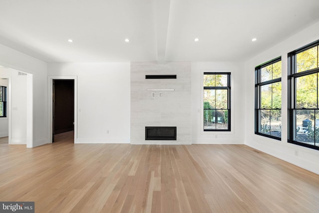 unfurnished living room featuring light hardwood / wood-style flooring, beam ceiling, and a fireplace