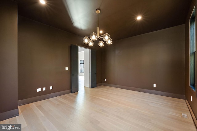 unfurnished room featuring a notable chandelier and light wood-type flooring