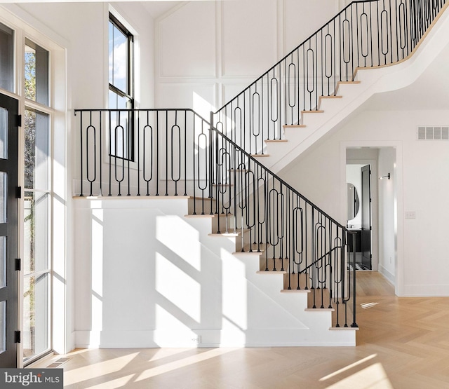 stairway with parquet floors and a towering ceiling