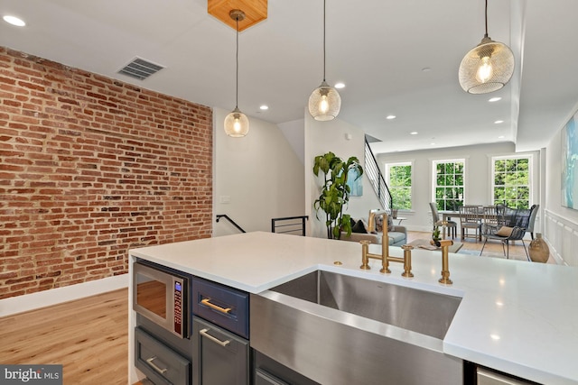 kitchen with pendant lighting, stainless steel microwave, sink, light wood-type flooring, and brick wall