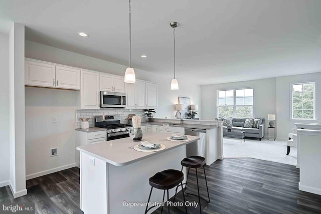 kitchen featuring a kitchen breakfast bar, kitchen peninsula, white cabinets, decorative light fixtures, and appliances with stainless steel finishes