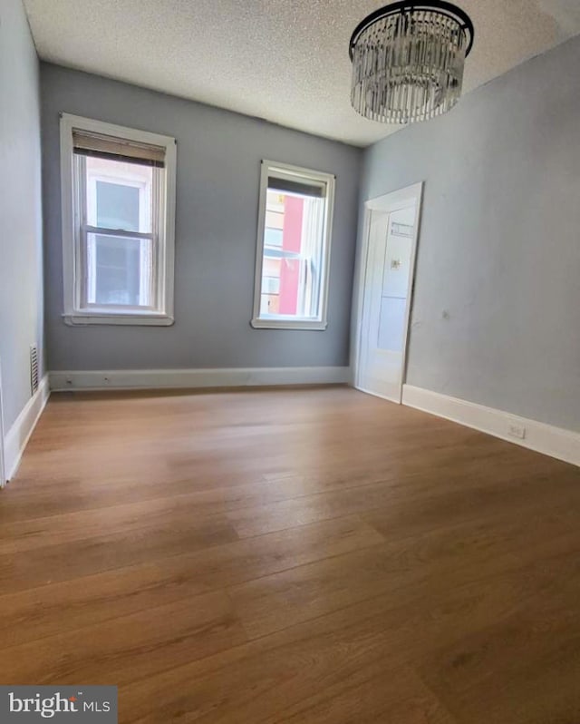 empty room with a textured ceiling, light hardwood / wood-style flooring, and an inviting chandelier