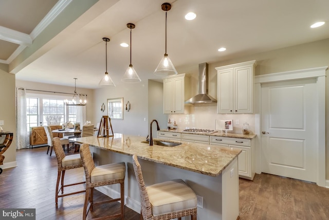 kitchen featuring wall chimney range hood, light stone counters, dark hardwood / wood-style flooring, pendant lighting, and sink