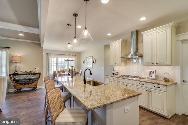 kitchen with an island with sink, light stone countertops, sink, wall chimney exhaust hood, and decorative light fixtures