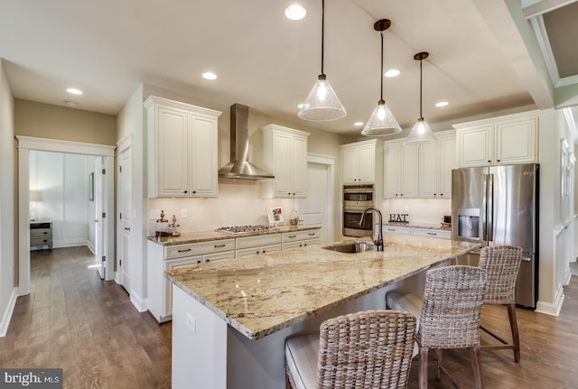 kitchen featuring a spacious island, stainless steel appliances, sink, wall chimney exhaust hood, and decorative light fixtures