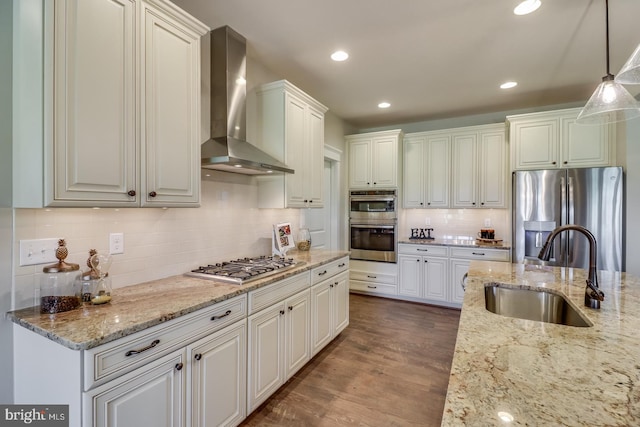 kitchen featuring wall chimney exhaust hood, hanging light fixtures, stainless steel appliances, sink, and white cabinets