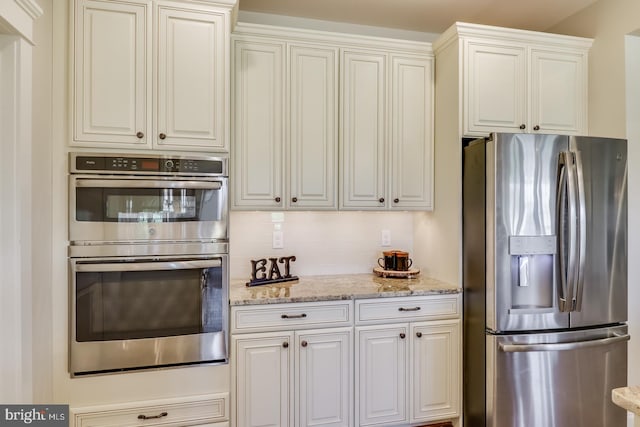 kitchen featuring backsplash, stainless steel appliances, light stone countertops, and white cabinets