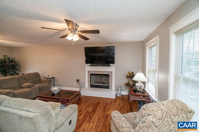 living room with ceiling fan, hardwood / wood-style flooring, a textured ceiling, and a tile fireplace