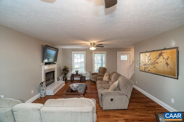 living room with a textured ceiling, a tiled fireplace, dark hardwood / wood-style floors, and ceiling fan