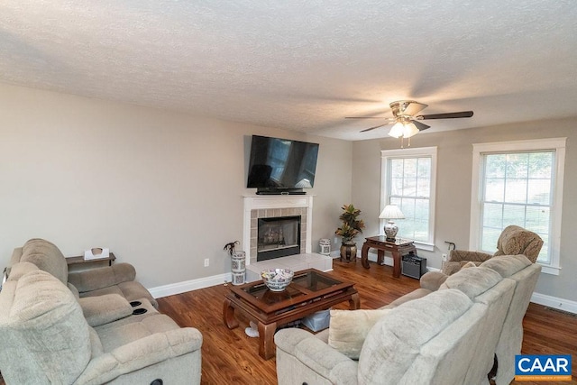 living room with a textured ceiling, hardwood / wood-style flooring, a tile fireplace, and ceiling fan