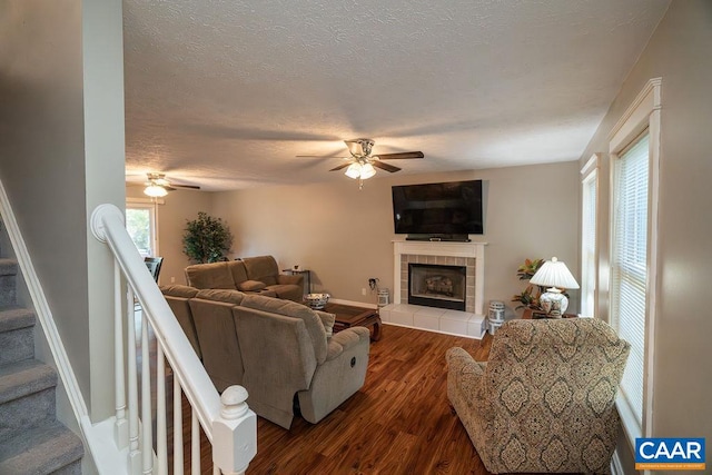 living room featuring a textured ceiling, ceiling fan, a tiled fireplace, and dark hardwood / wood-style flooring