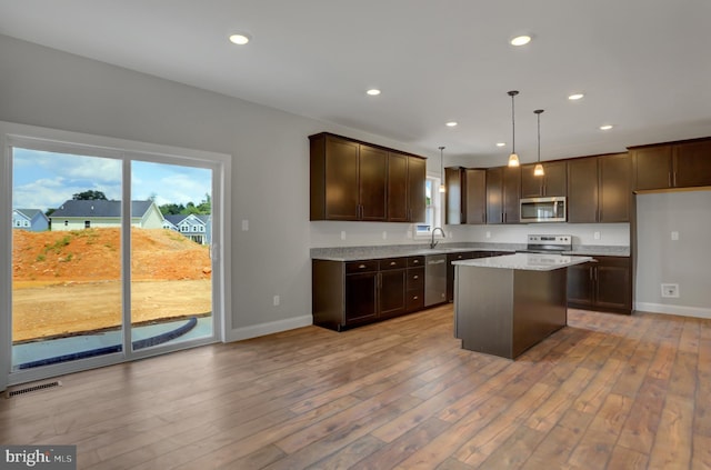 kitchen featuring light stone counters, stainless steel appliances, pendant lighting, light hardwood / wood-style floors, and a center island