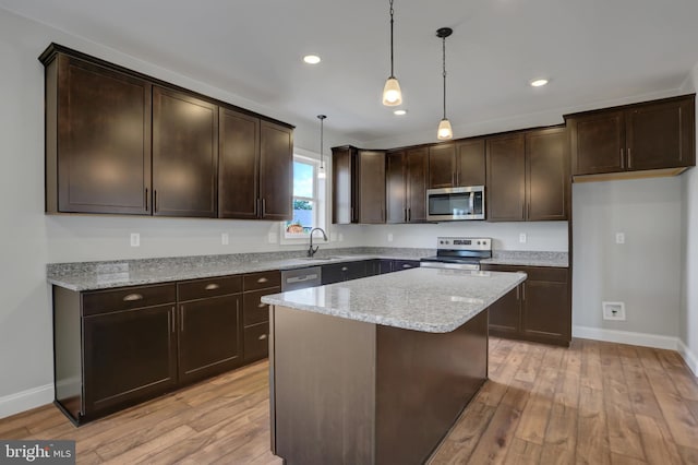 kitchen featuring light hardwood / wood-style flooring, appliances with stainless steel finishes, decorative light fixtures, and a kitchen island