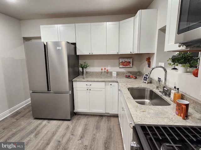 kitchen with white cabinets, sink, light hardwood / wood-style flooring, light stone countertops, and appliances with stainless steel finishes