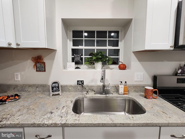 kitchen with stainless steel range, light stone countertops, sink, and white cabinets