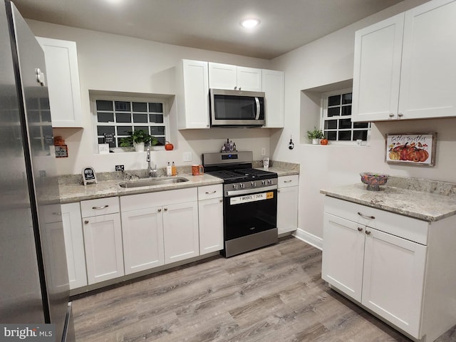 kitchen with light wood-type flooring, light stone counters, stainless steel appliances, sink, and white cabinets