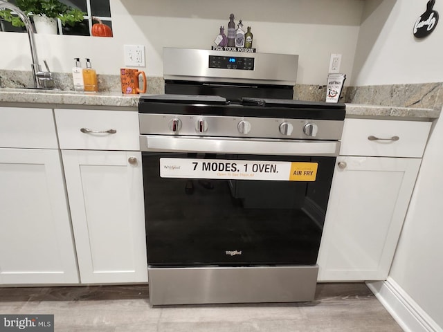 kitchen with white cabinets, light stone countertops, sink, and stainless steel stove