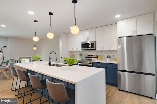 kitchen with a center island with sink, appliances with stainless steel finishes, blue cabinetry, decorative light fixtures, and sink