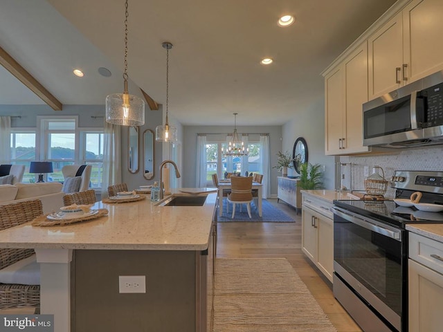 kitchen with light hardwood / wood-style floors, sink, an island with sink, appliances with stainless steel finishes, and decorative light fixtures