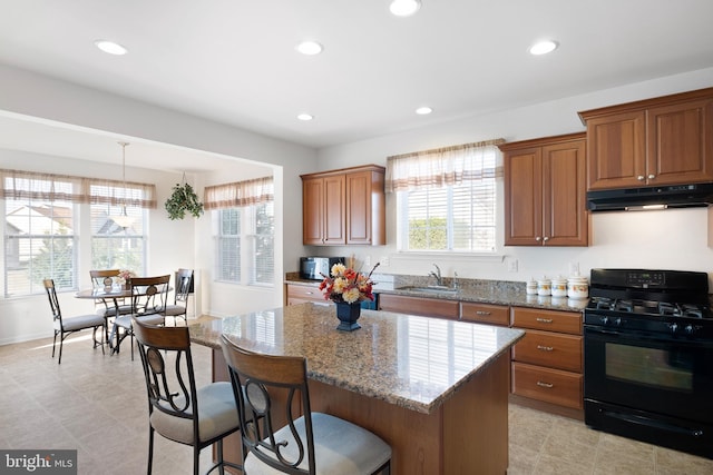 kitchen featuring black appliances, sink, a center island, decorative light fixtures, and light stone counters