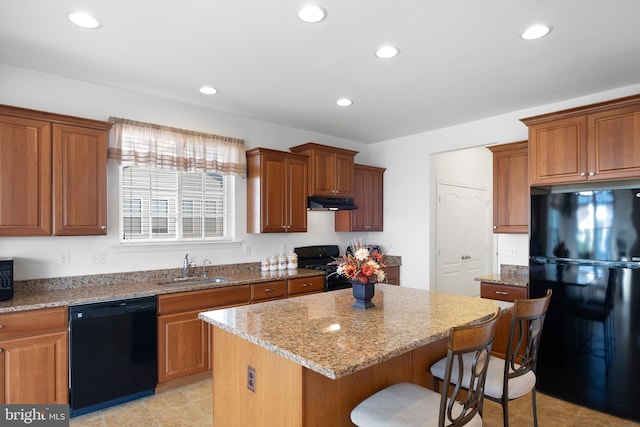 kitchen with sink, light stone countertops, black appliances, a center island, and a kitchen bar