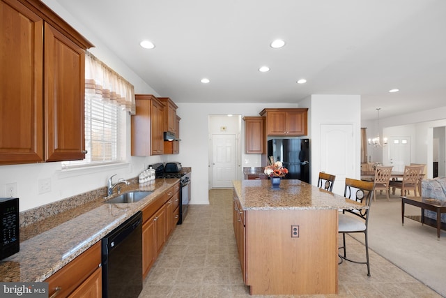 kitchen featuring a kitchen island, a kitchen breakfast bar, light stone countertops, black appliances, and sink