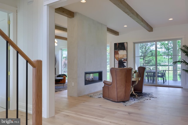 living area with light hardwood / wood-style flooring, beam ceiling, and a large fireplace