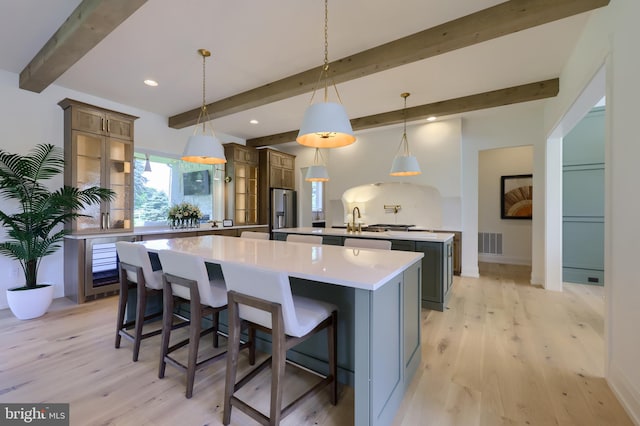 kitchen with a spacious island, beam ceiling, stainless steel refrigerator with ice dispenser, decorative light fixtures, and light hardwood / wood-style floors