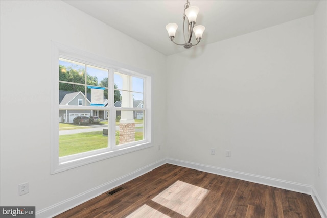 spare room featuring an inviting chandelier and dark hardwood / wood-style floors