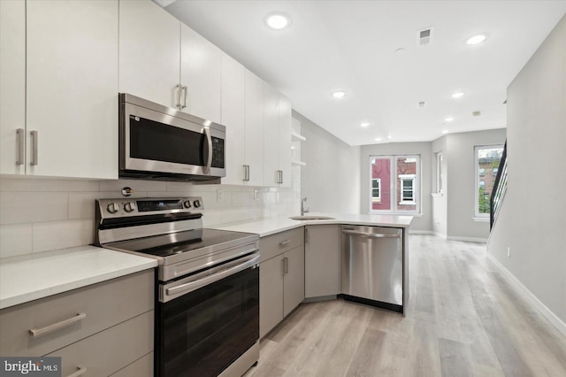 kitchen featuring tasteful backsplash, sink, kitchen peninsula, stainless steel appliances, and light hardwood / wood-style flooring